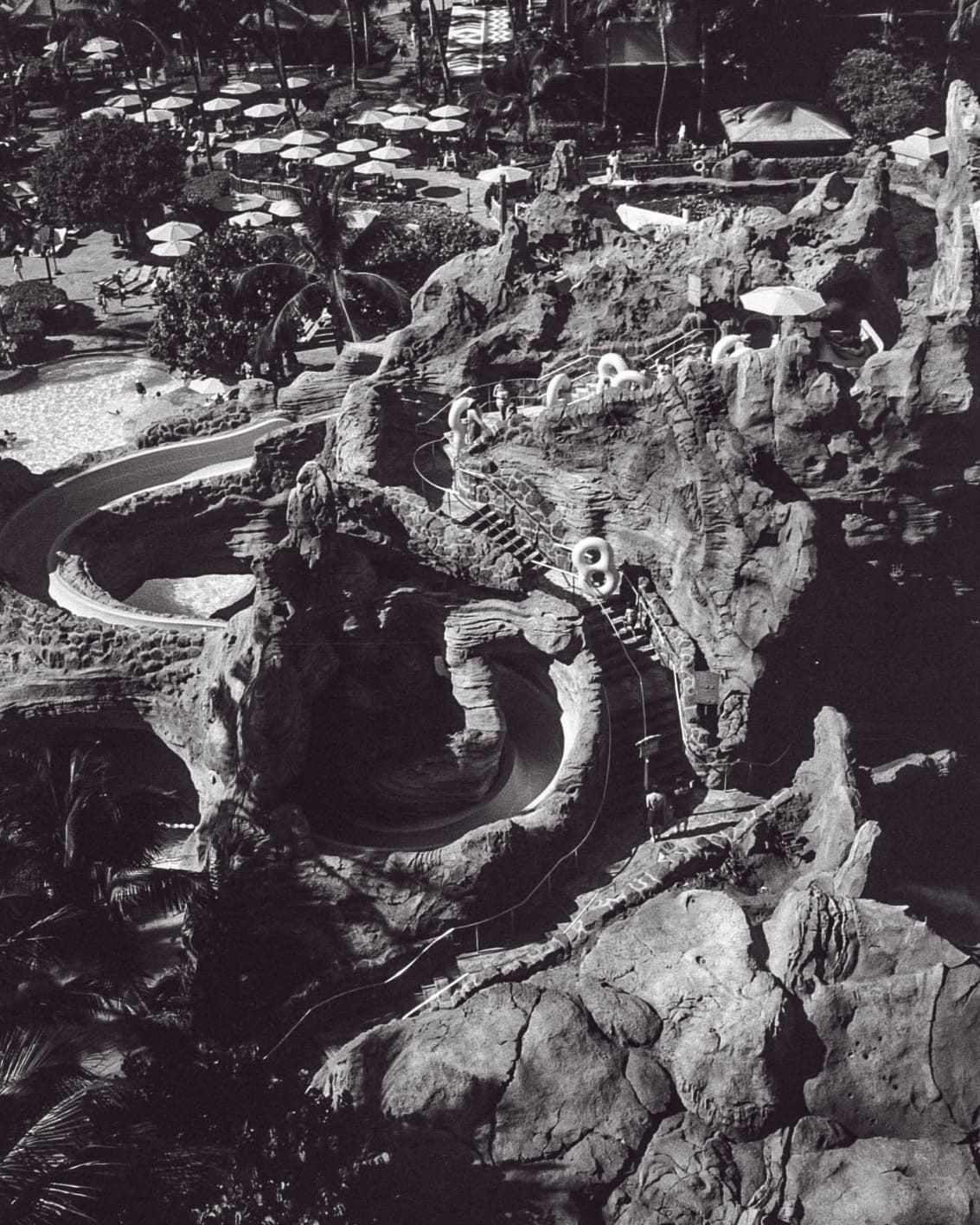 An aerial view shows a water park with slides, pools, and umbrellas.