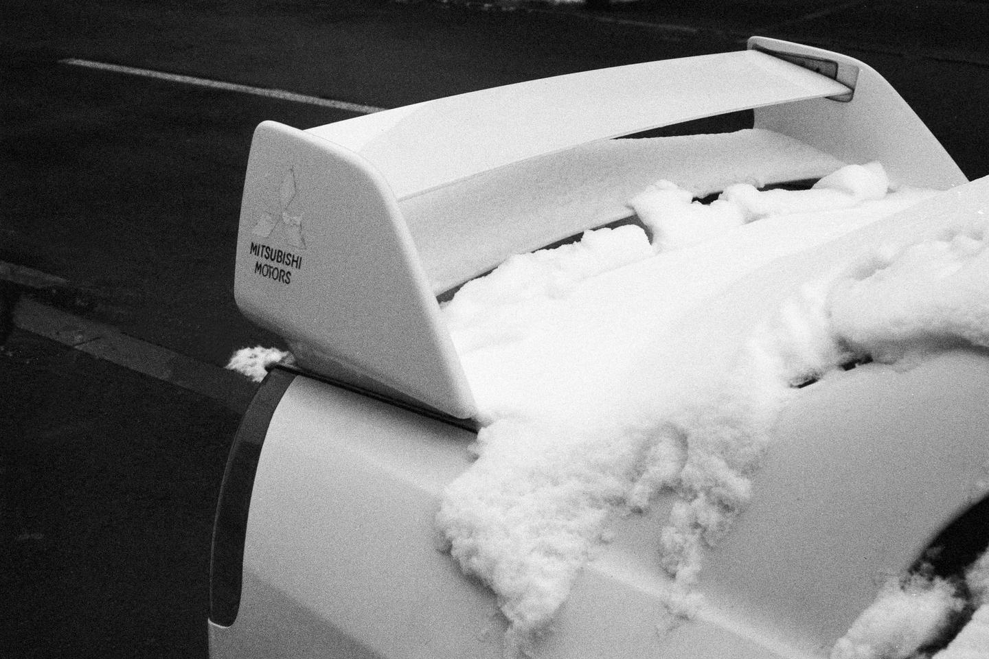 A white car with a spoiler is covered in snow.