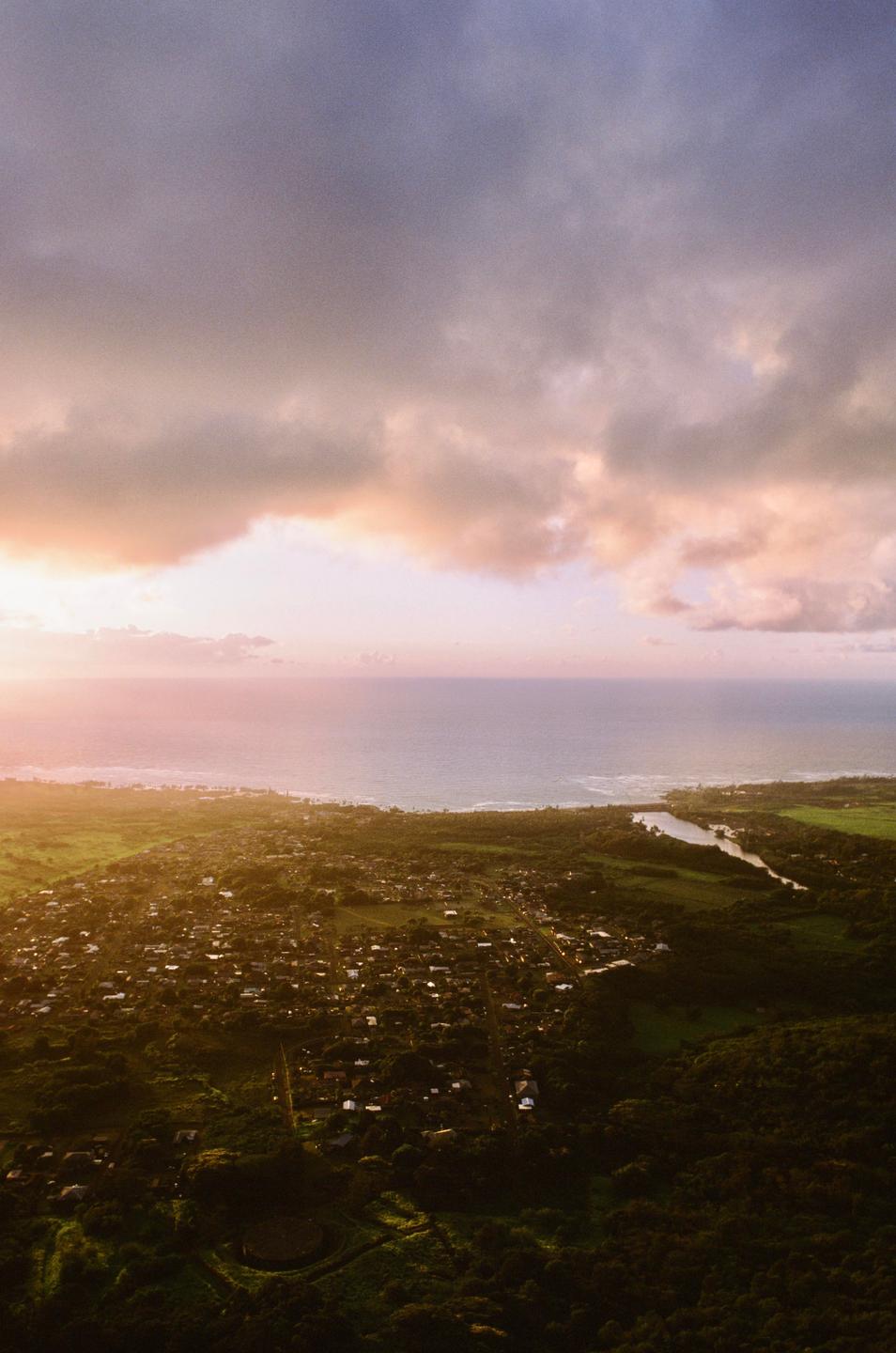 An aerial view shows a coastal town nestled between lush green landscapes and the ocean under a dramatic sky.