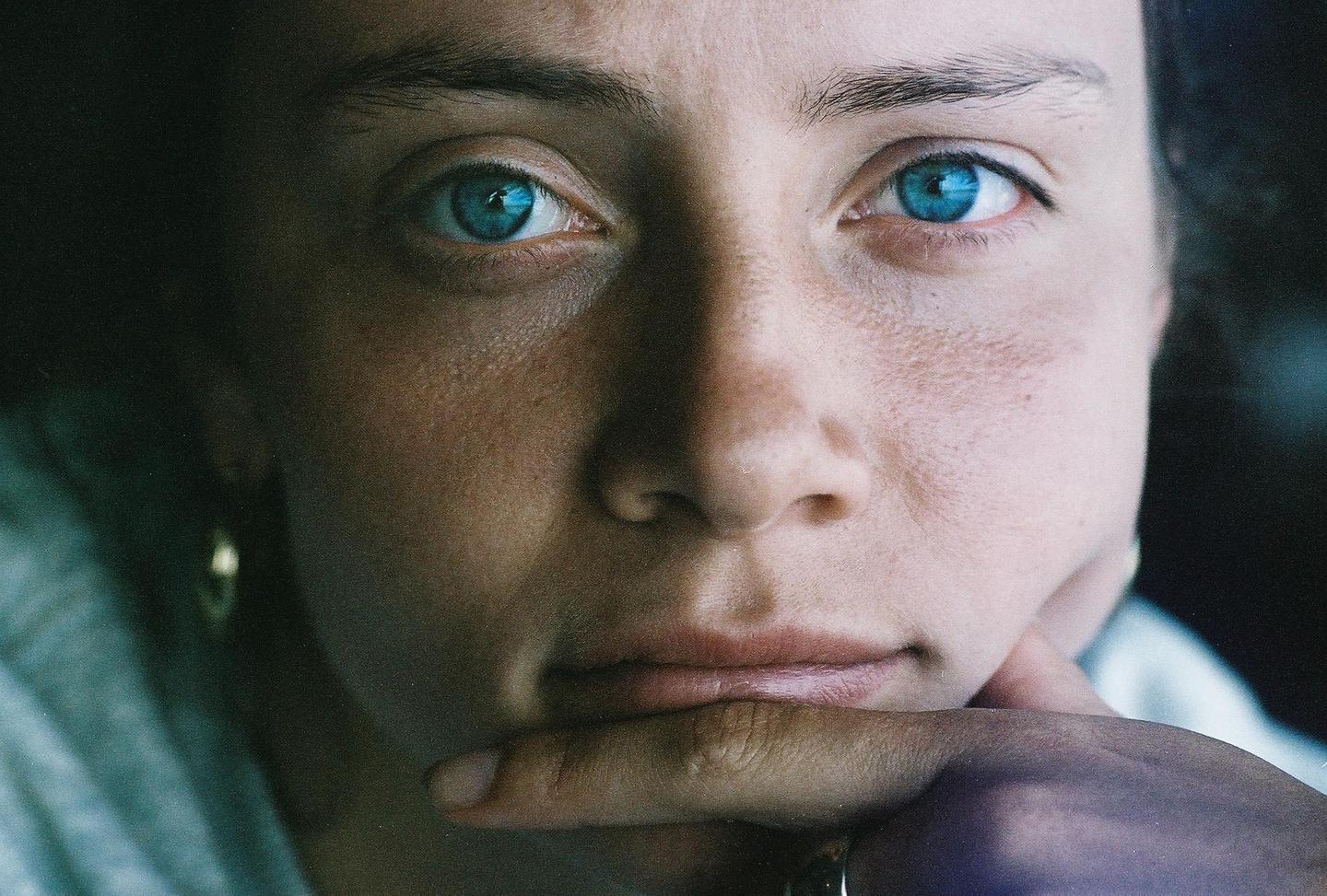 A woman with striking blue eyes rests her chin on her hand.
