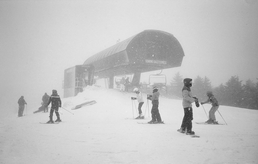 Skiers stand in the snow near a ski lift during a snowstorm.