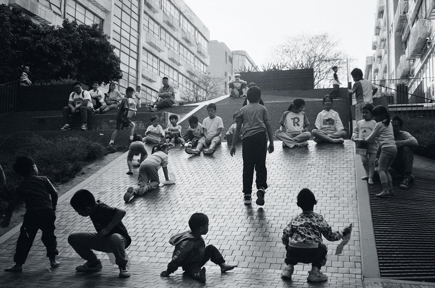 A group of children and adults are gathered on a paved incline next to a building.