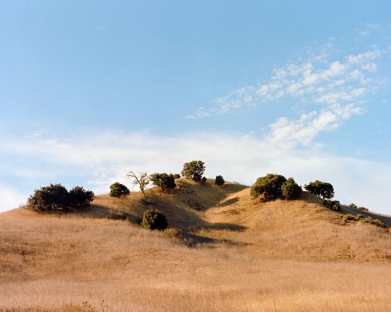 A golden hill with scattered trees is visible under a blue sky with wispy clouds.