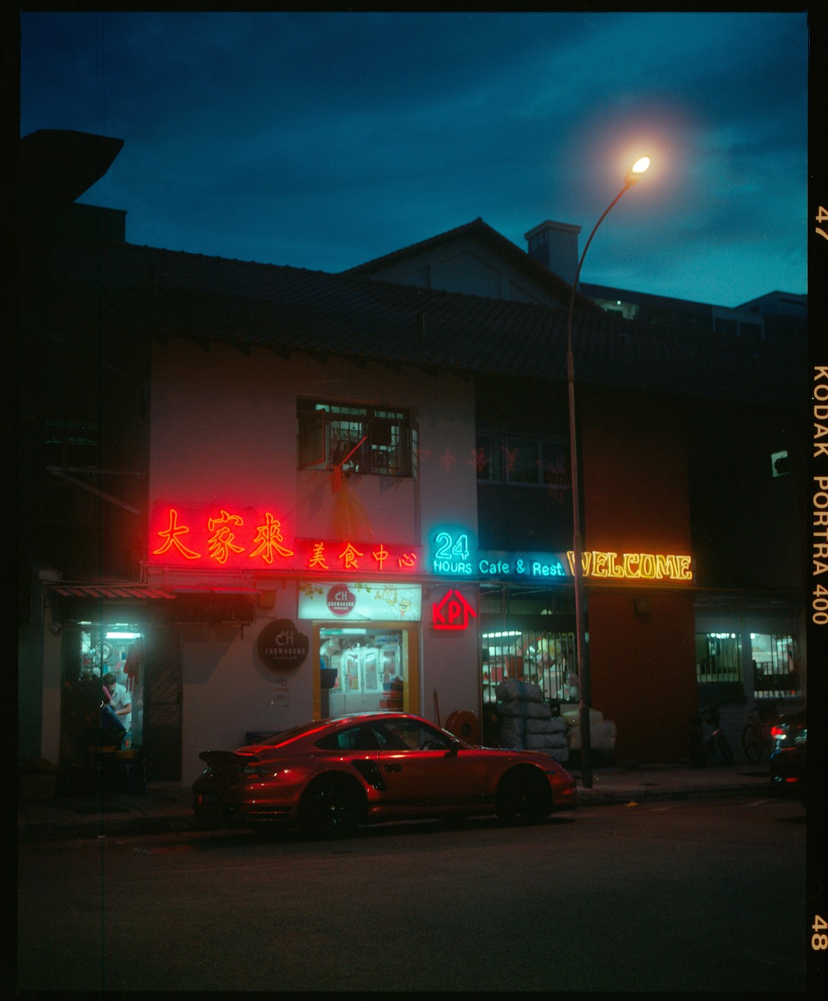 A red sports car is parked on a street in front of a building with neon signs at night.