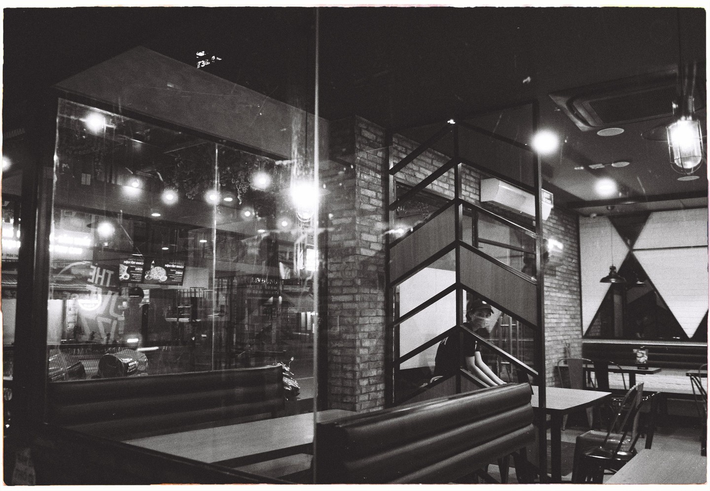 A person sits on a staircase inside a restaurant at night, visible through a glass window.