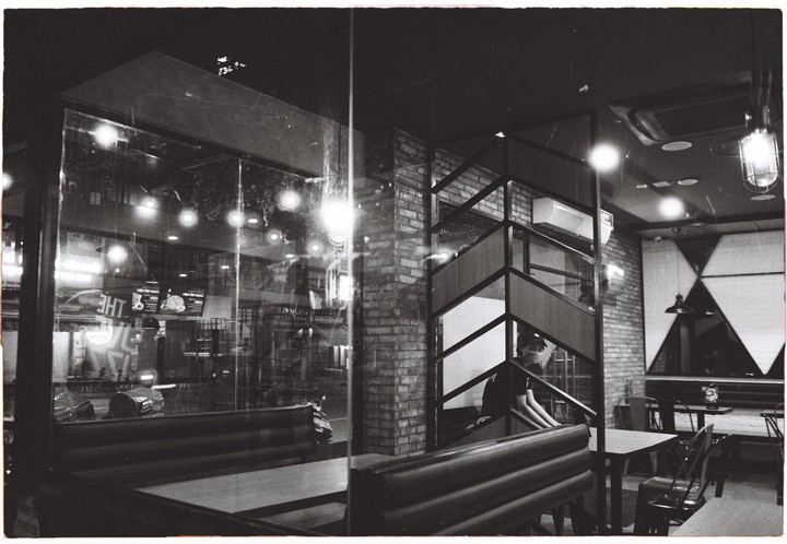 A person sits on a staircase inside a restaurant at night, visible through a glass window.