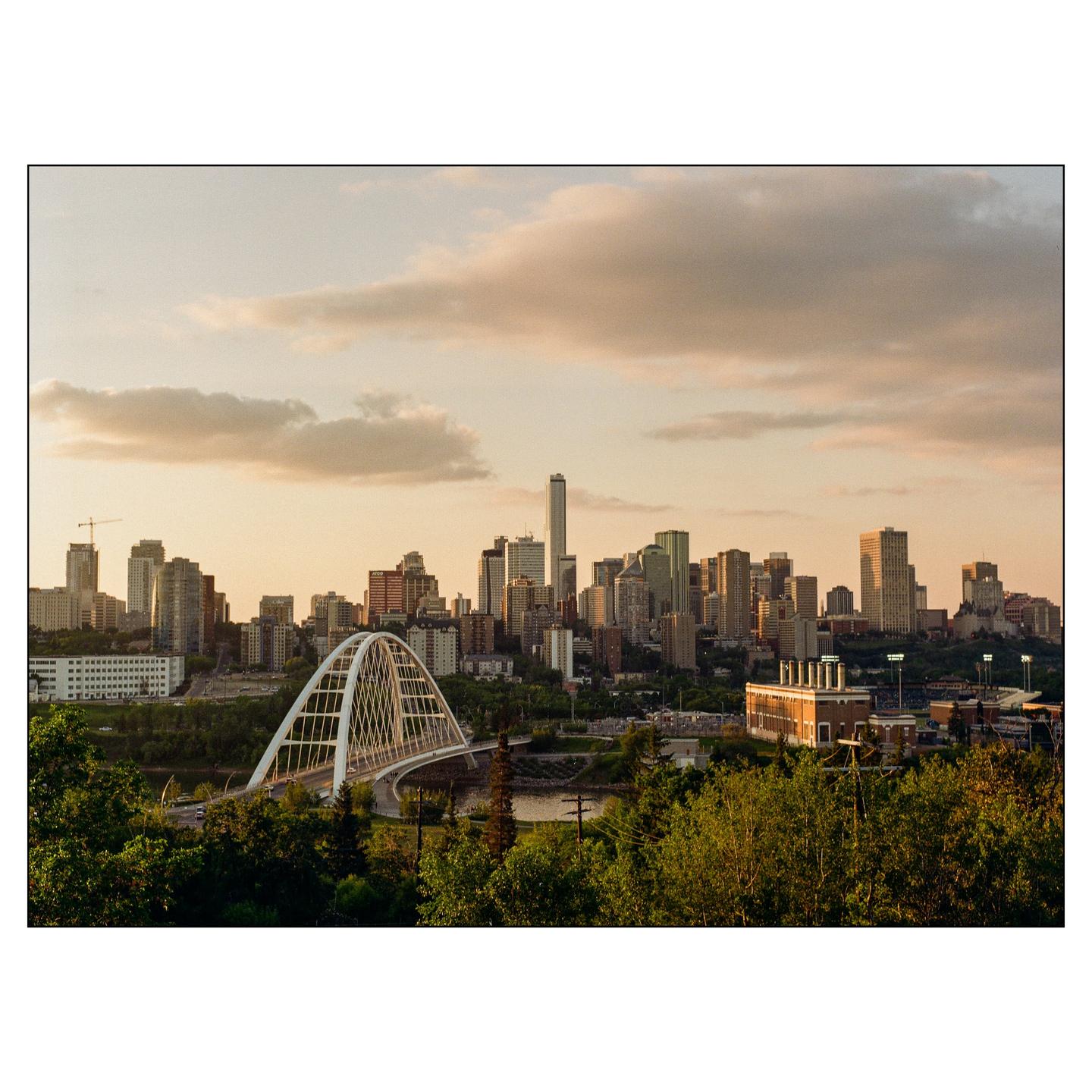 A city skyline with a prominent arched bridge over a river is visible at sunset.