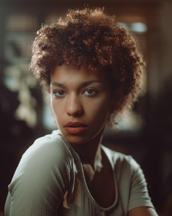 A woman with curly hair looks directly at the viewer.