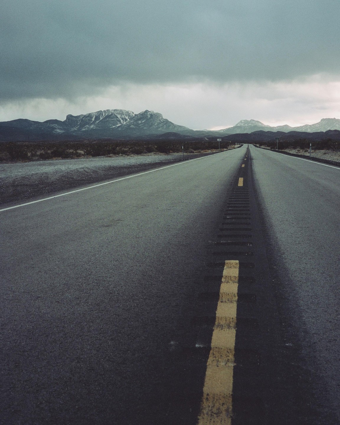 A long road stretches towards distant mountains under a cloudy sky.