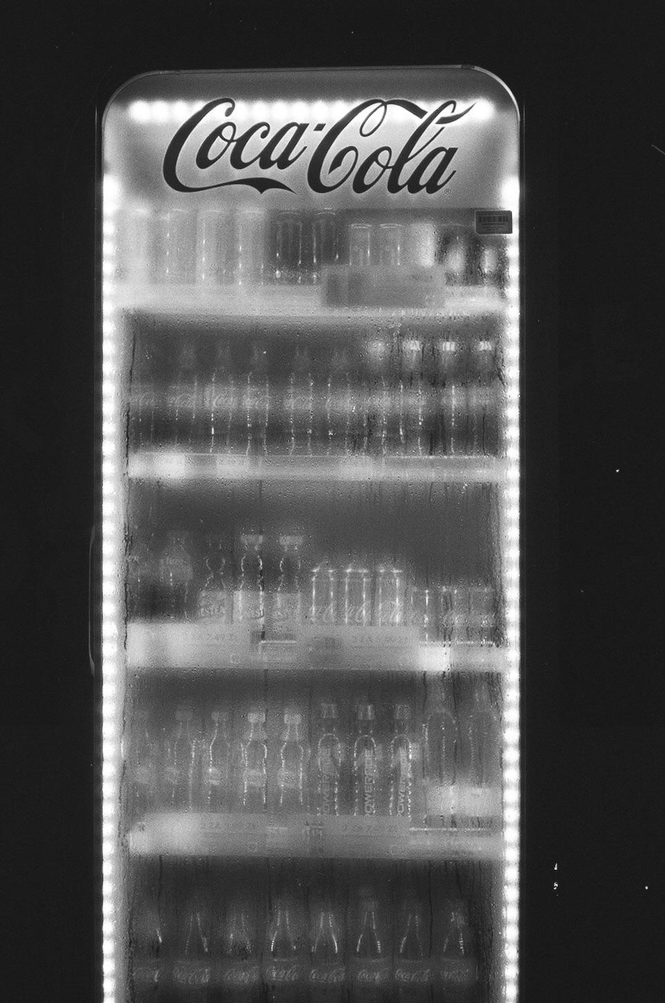 A Coca-Cola refrigerator is filled with bottles and illuminated by internal lights.