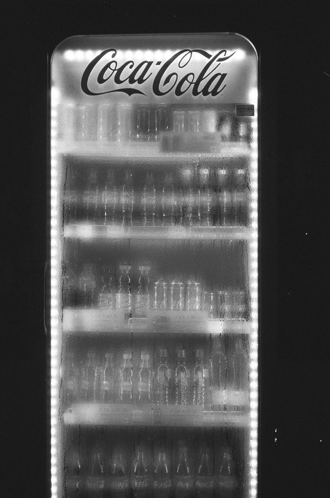 A Coca-Cola refrigerator is filled with bottles and illuminated by internal lights.