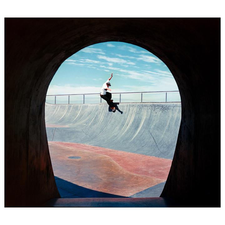 A skateboarder is captured mid-air in a skate park, framed by a dark, arched tunnel.