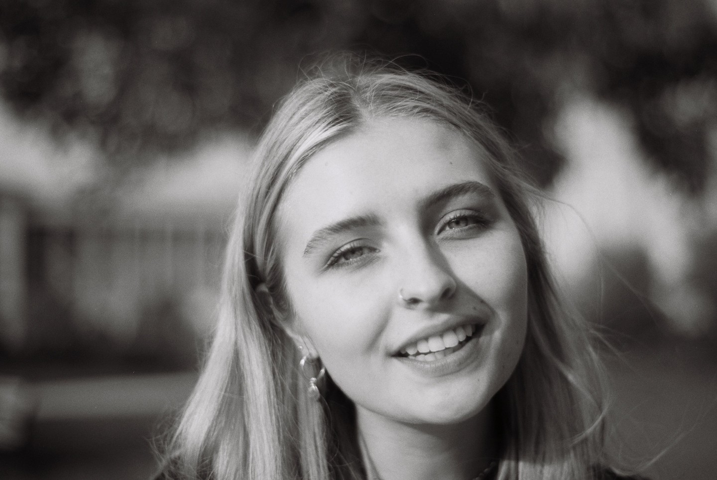 A young woman with long hair and a nose ring smiles at the viewer.
