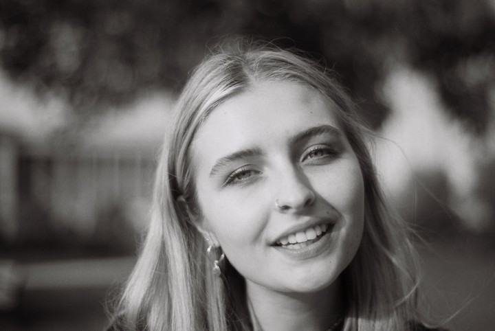 A young woman with long hair and a nose ring smiles at the viewer.