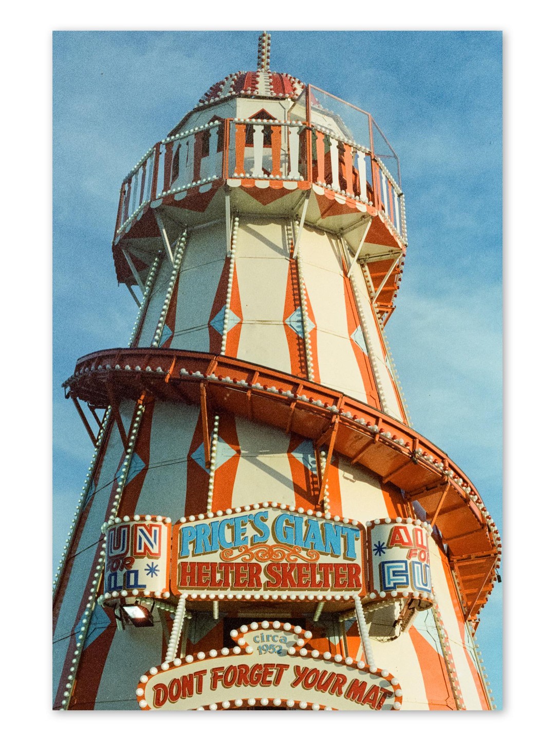 A helter skelter ride with red and white stripes stands against a clear blue sky.