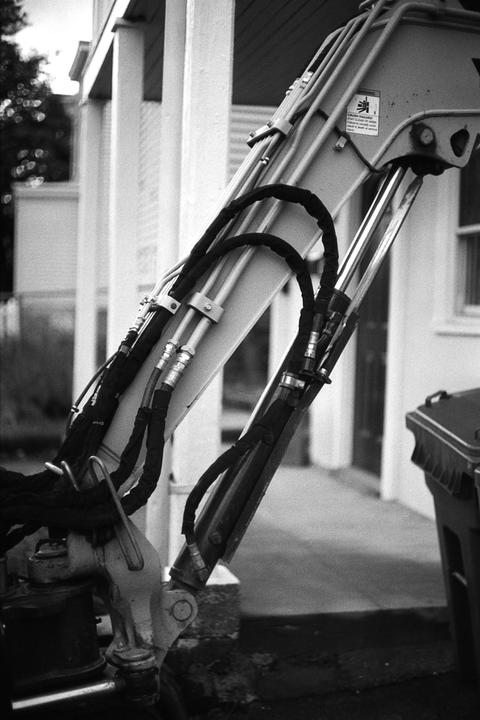A close-up view shows the hydraulic arm of an excavator with hoses and cylinders.