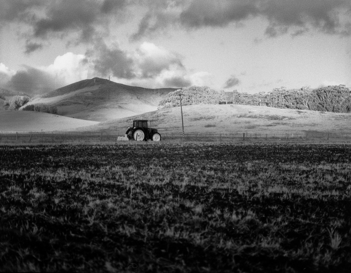 A tractor is parked in a field with hills and trees in the background under a cloudy sky.