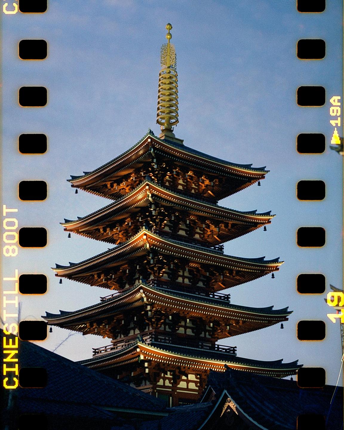 A five-storied pagoda with a golden spire stands against a clear sky.