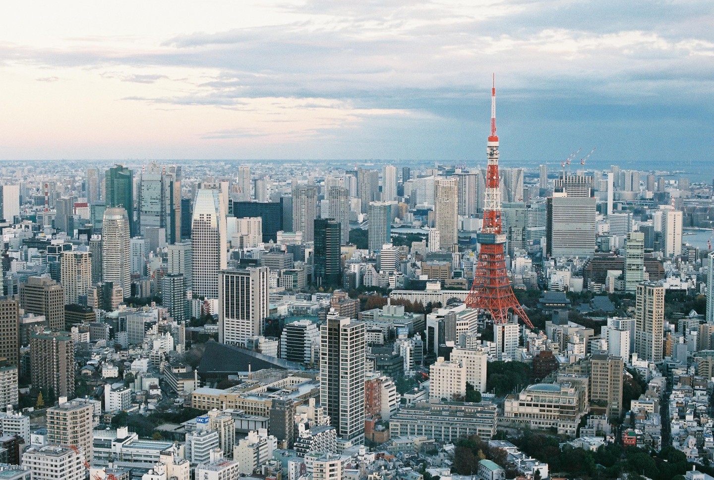 An aerial view of Tokyo shows the city's dense urban landscape with numerous skyscrapers and the Tokyo Tower prominently featured.