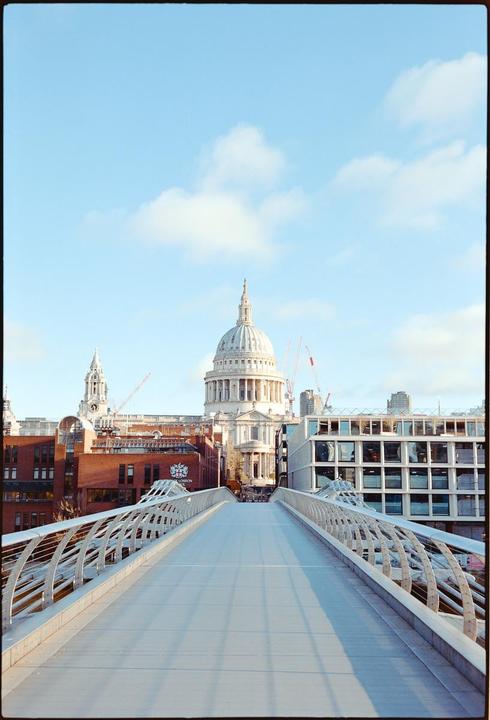 A wide pedestrian bridge leads towards St. Paul's Cathedral under a bright sky with scattered clouds.