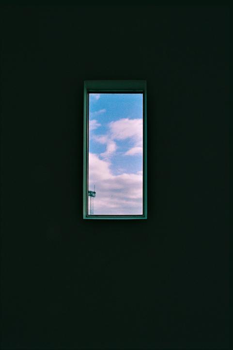 A small rectangular window shows a blue sky with white clouds and a distant structure.