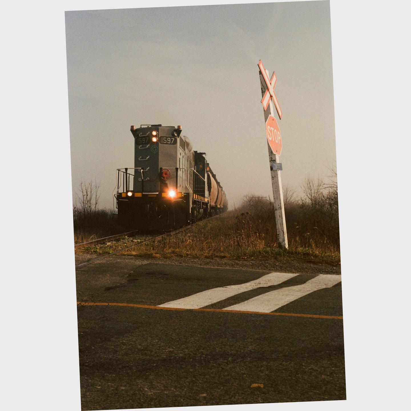 A train approaches a railroad crossing with a stop sign and a crossbuck sign.