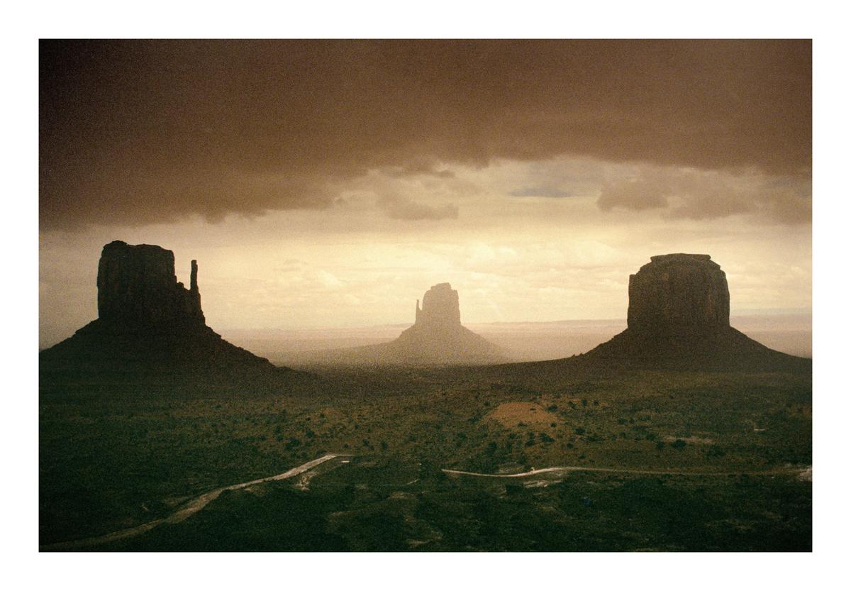 Three large rock formations stand in a desert landscape under a cloudy sky.