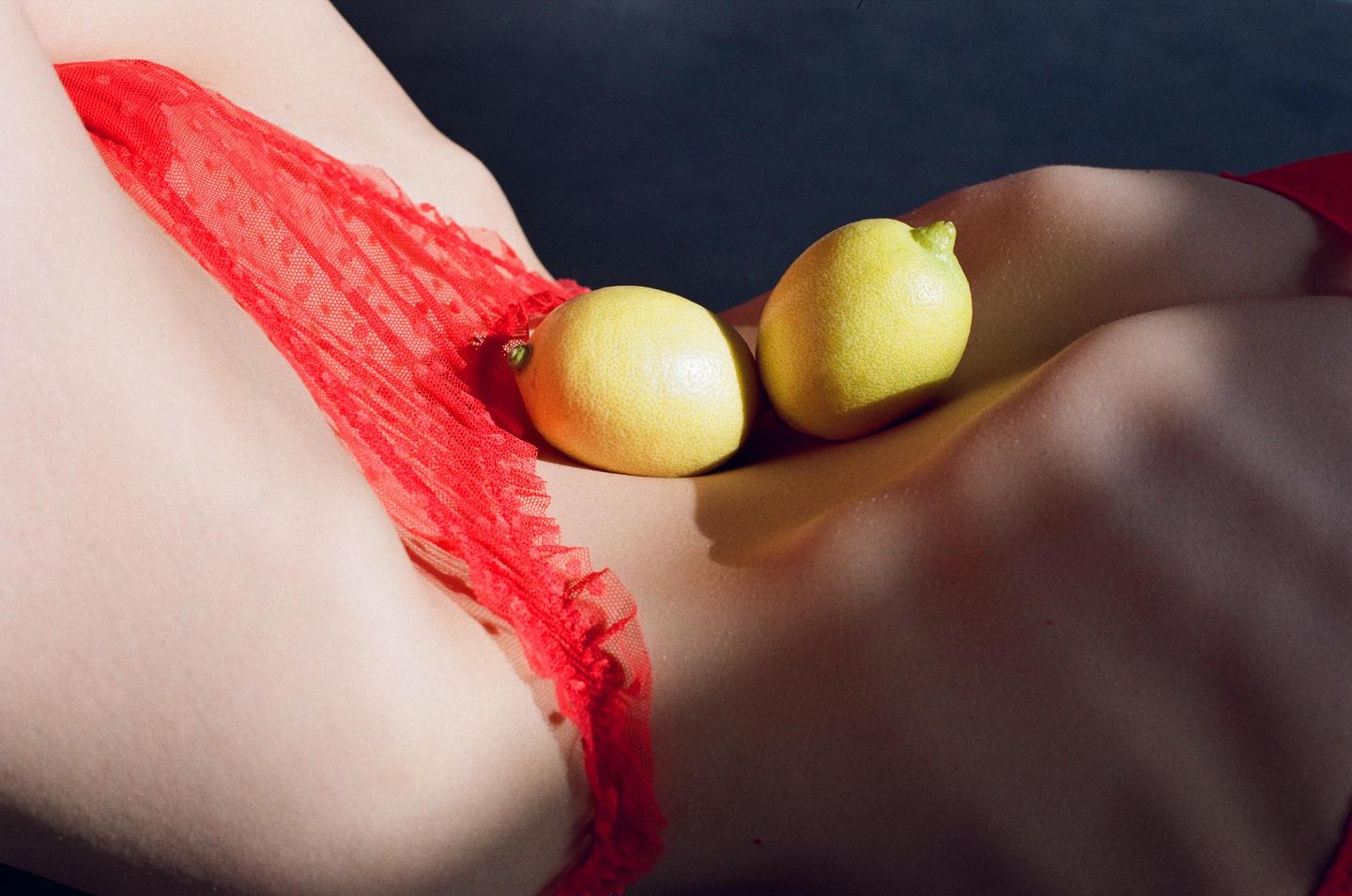 Two lemons rest on a person's stomach, partially covered by red lace underwear.