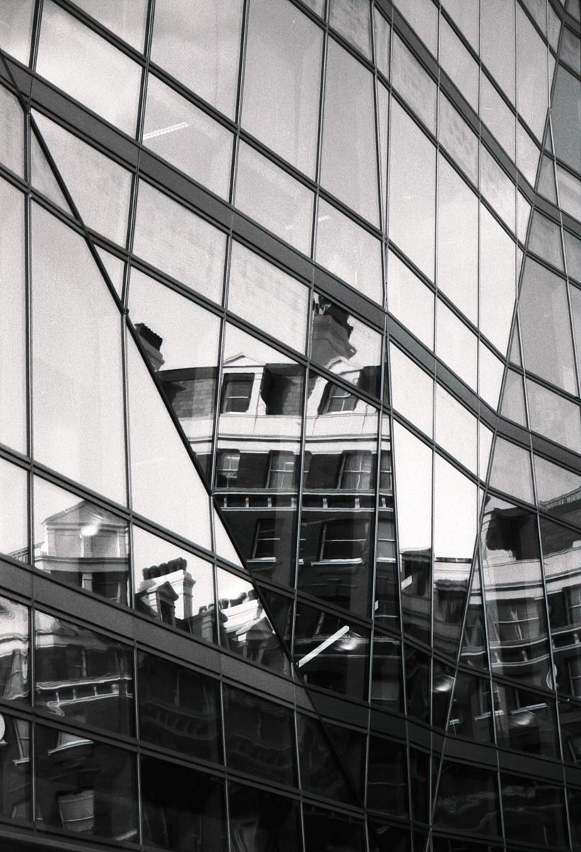 An old building is reflected in the glass facade of a modern building.