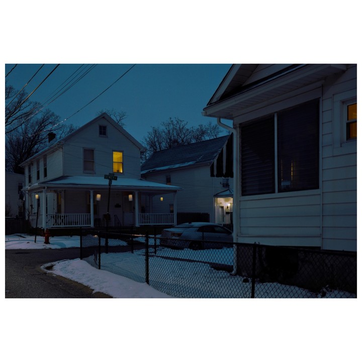 A street corner with houses and a car is covered in snow at night.