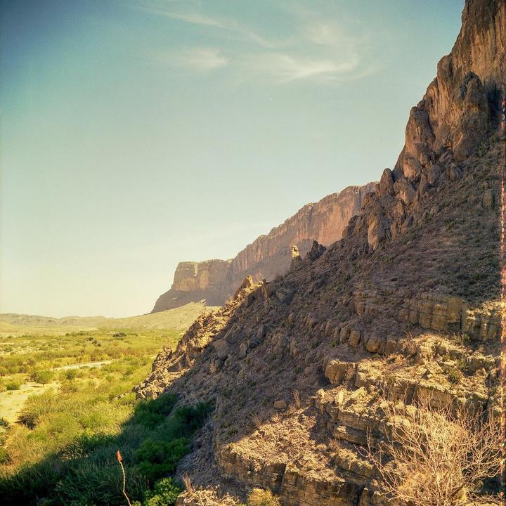 A vast desert landscape features a rocky mountain range under a clear sky.