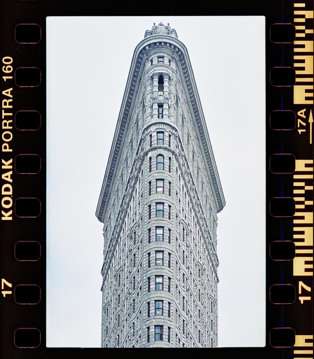 The Flatiron Building stands tall against a bright sky, captured with the film border visible.
