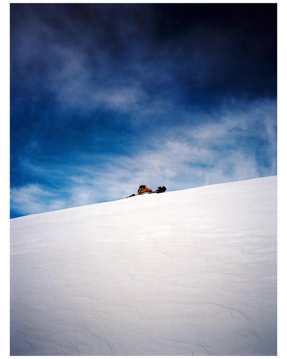 A snowcat is parked on a snow-covered hill under a dramatic blue sky.