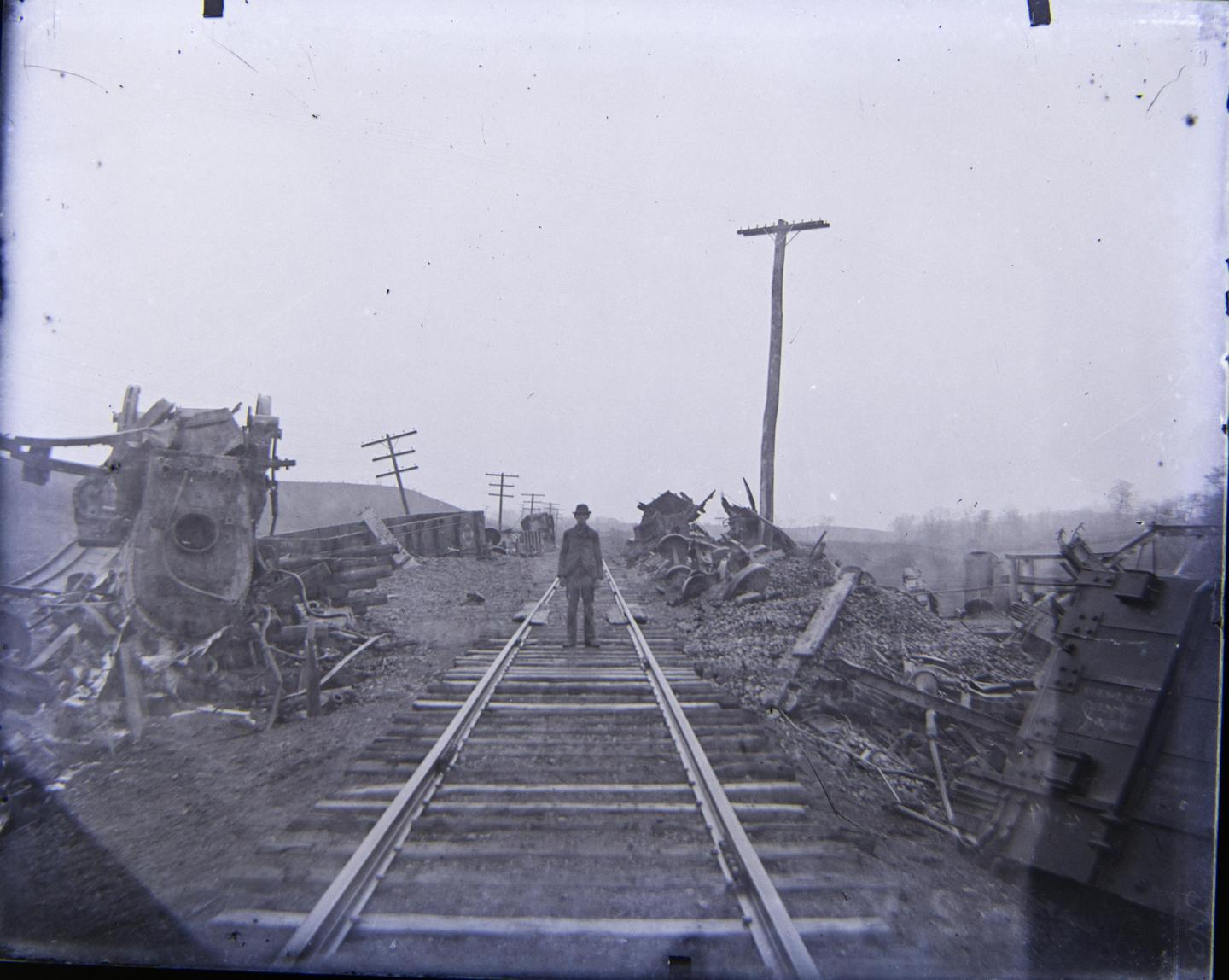 A man stands on train tracks surrounded by the wreckage of a train derailment.