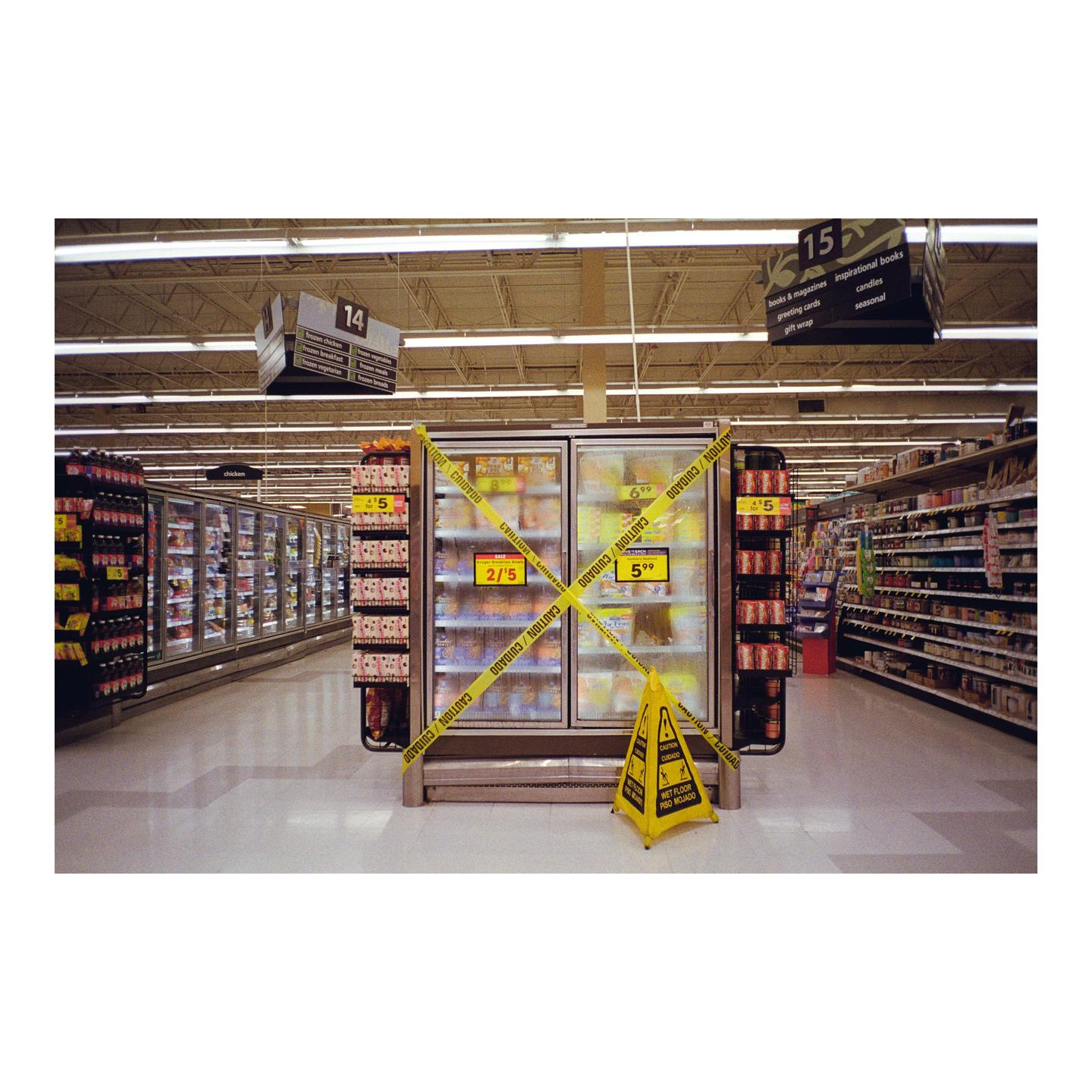 A yellow caution tape is wrapped around two refrigerators in a grocery store aisle.