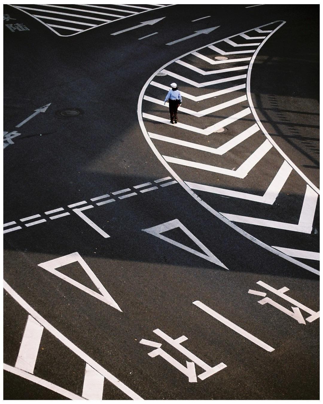 A man in a uniform walks on a street with white road markings and Chinese characters.