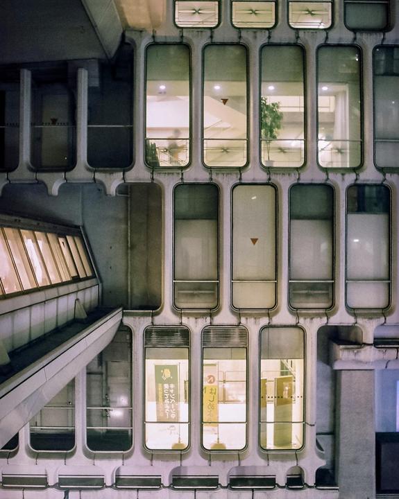 A building with many small, rounded rectangular windows is illuminated at night.