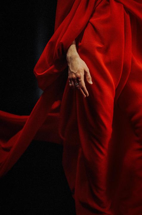 A person's hand with rings is visible against a flowing red fabric.