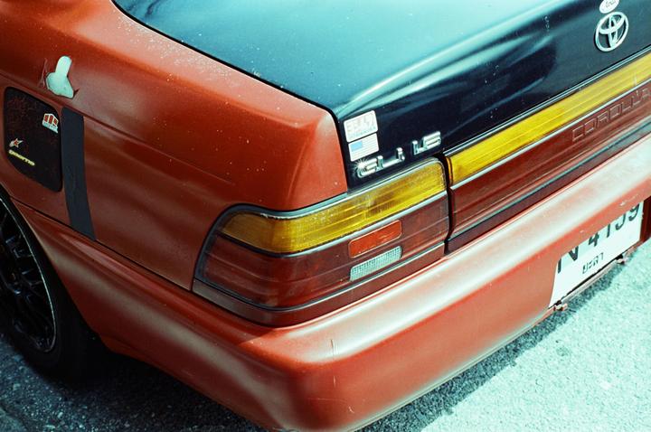 The back of a red Toyota Corolla is visible, with a black trunk and yellow and red taillights.