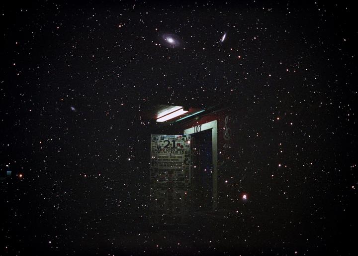 A dark night sky filled with stars and galaxies is visible above a building entrance with a sign.