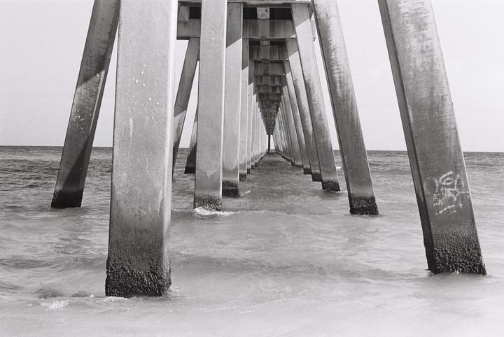 The concrete pillars of a pier extend into the distance over the ocean.