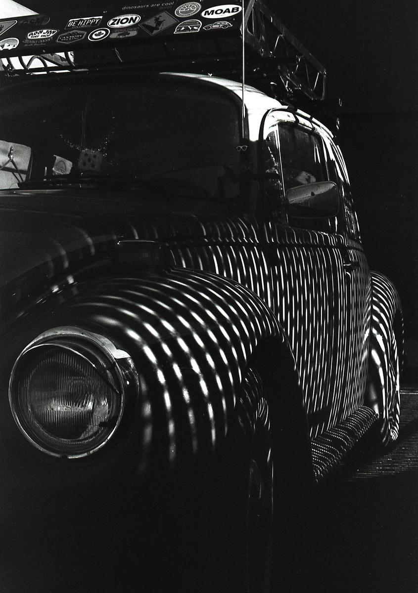 A Volkswagen Beetle is parked with striped shadows cast across its body.