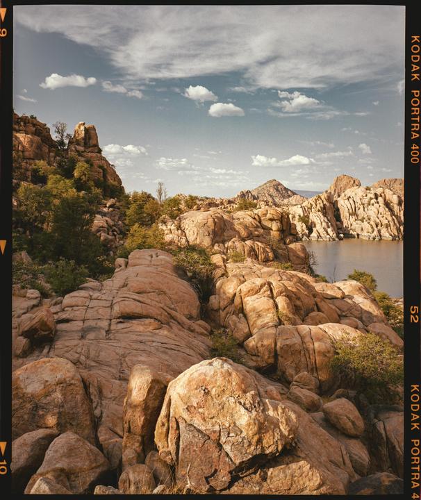 A body of water is surrounded by large, textured rock formations and green foliage under a partly cloudy sky.