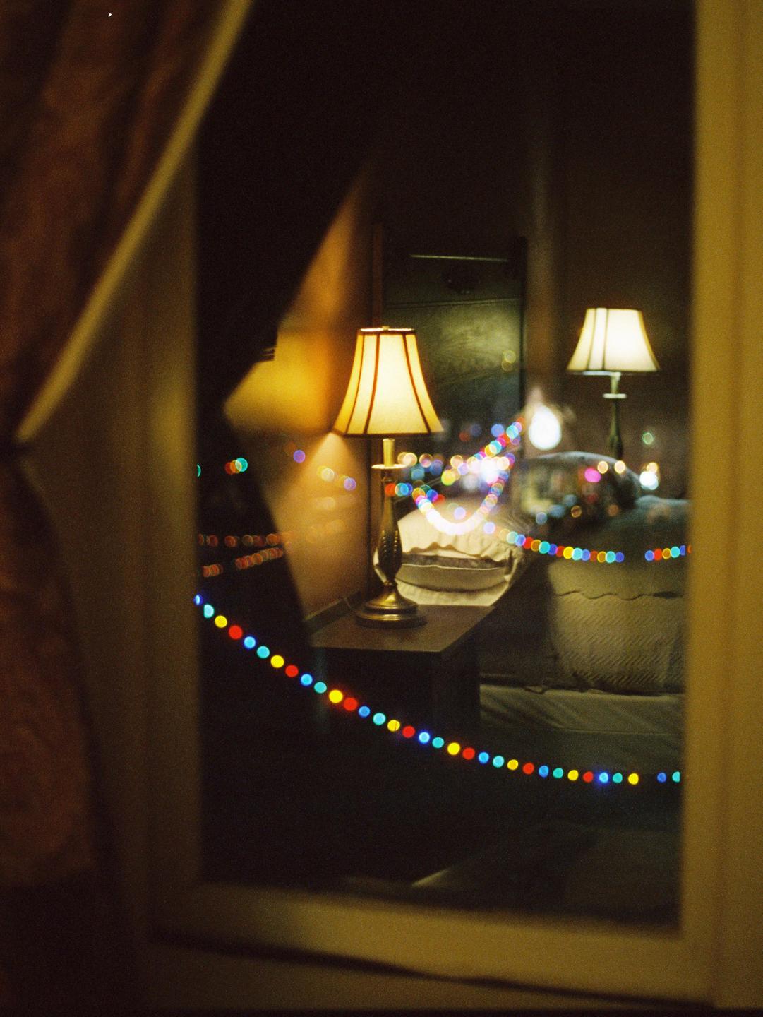 Two lamps illuminate a room with colorful string lights reflected in a window.