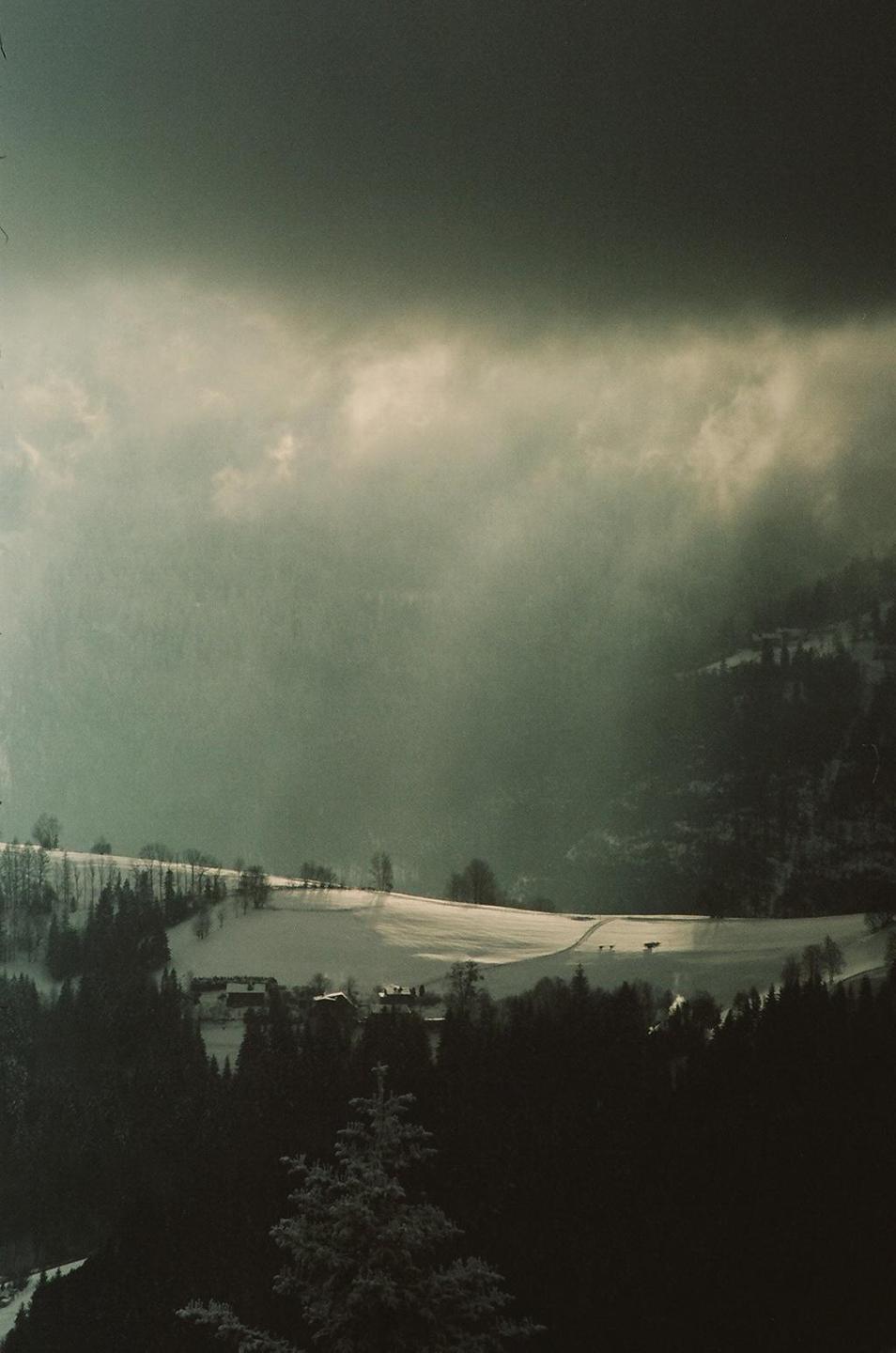 A snow-covered valley with houses and trees is visible under a cloudy sky.