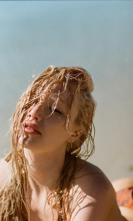 A woman with wet, blonde hair looks up with her eyes closed, her face partially shadowed.