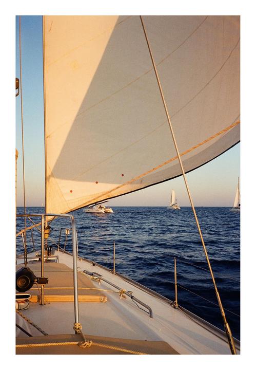 A sailboat with a large white sail is on the water with other boats in the distance.
