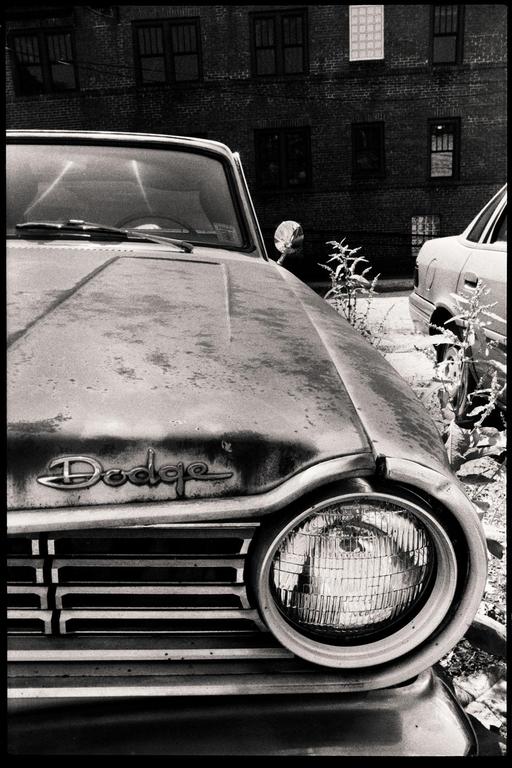 A close-up view of the front of an old Dodge car with a brick building in the background.