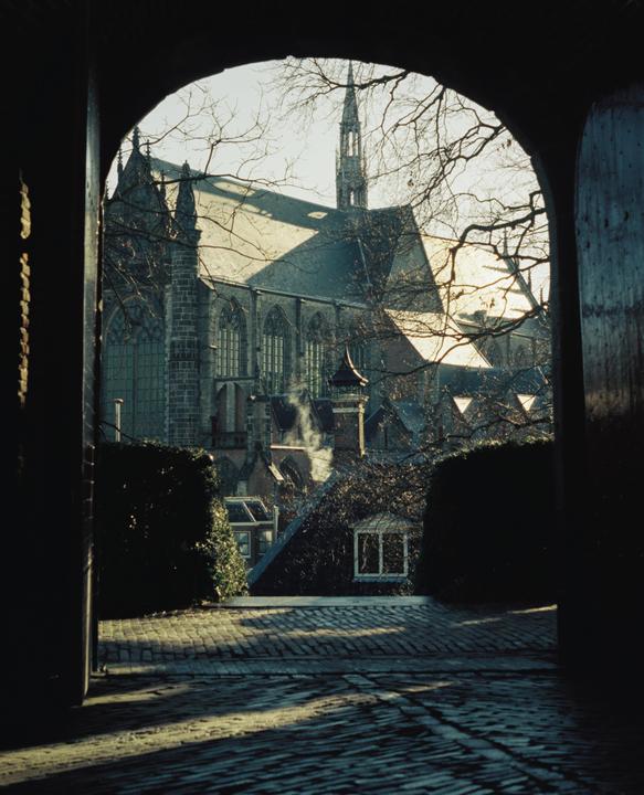 A large stone church with a tall spire is visible through an arched doorway, with cobblestones and rooftops in the foreground.