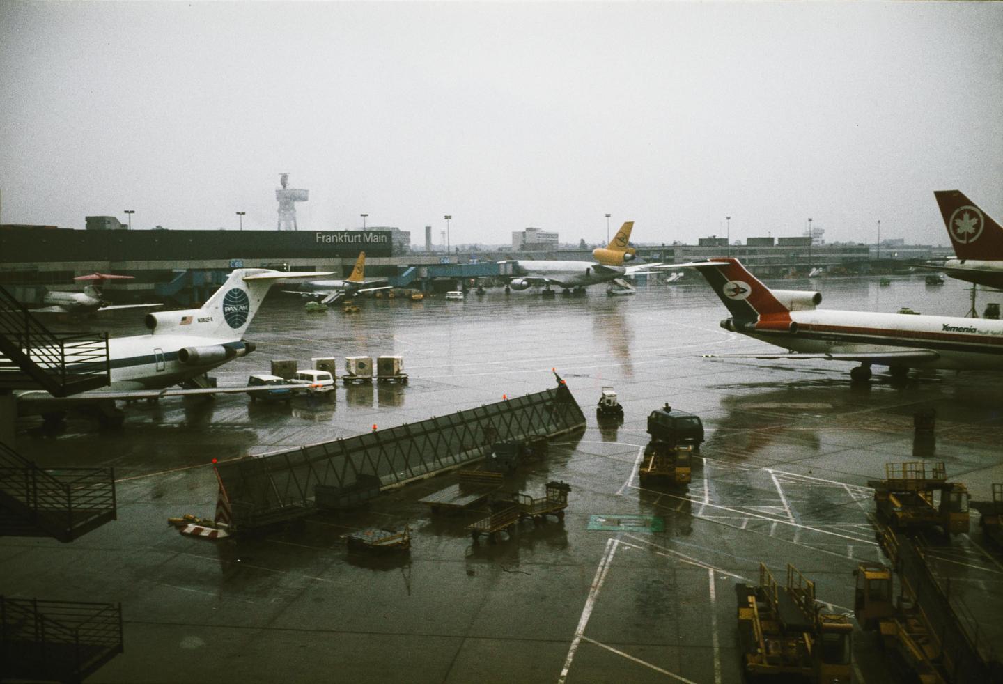 Airplanes are parked on a wet tarmac at Frankfurt Main airport.